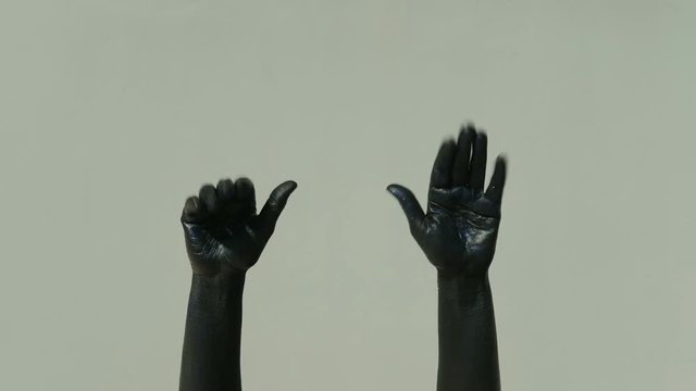 Actor mime with black hands shows gesture goodbye on a gray background. Palms in shiny paint in blue tint flex and unbend fingers slowly. The limbs are stretched and pantomime moves. When parting for