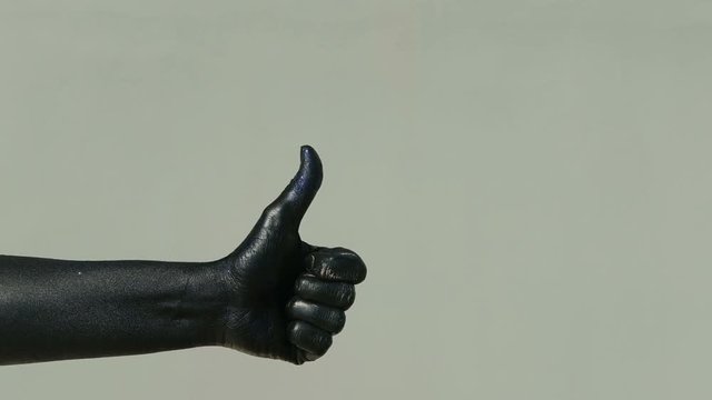 Mim with his black hand shows a raised thumb on his outstretched hand. The actor with a brilliant dark coating with a blue tint exposes the limb on which the fingers are stacked together, and the big