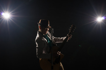 Asian Musician  singing a song and playing the guitar which have a microphone on black background with spot light and lens flare, musical concept