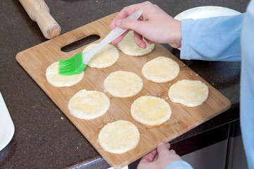 The girl smears cookies with beaten eggs in the kitchen.