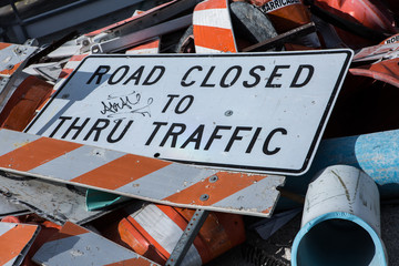 A dump of Road Closed Sign fell down on a road with broken barricades pile of metal and pipes close...