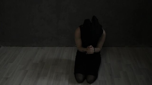 frightened crying girl gagged, lies on the floor with tied hands. linen bag on the head of a hostage. kidnapping and violence