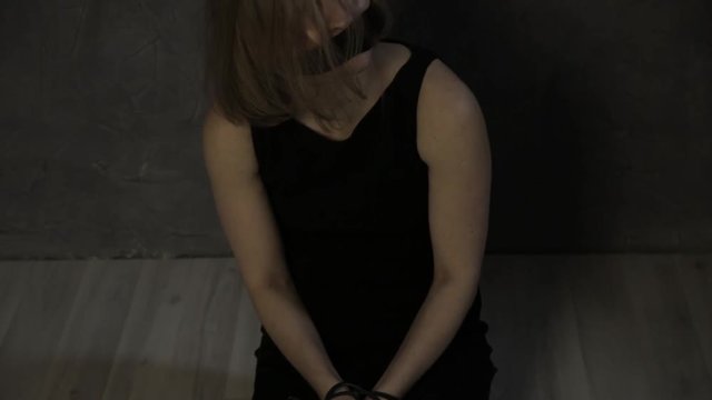 frightened crying girl gagged, lies on the floor with tied hands. linen bag on the head of a hostage. kidnapping and violence