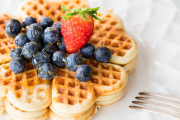 Fresh homemade heart shape waffles with blueberries and strawberry on white plate