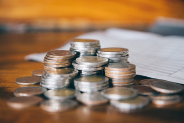 pile of money coins with blured salary slip on wood background