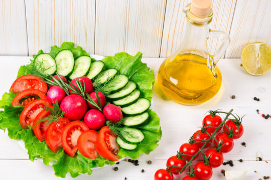 Cucumbers, radish, tomatoes cherry, olive oil, herb and spices on old white wooden background. Set for healthy foods. Ingredients for salad