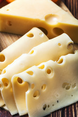Cheese in a hole on a wooden table. Maasdam, cheddar or other kind of cheese