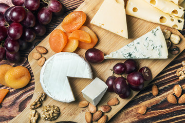 Assorted cheeses with grapes and nuts on a wooden table