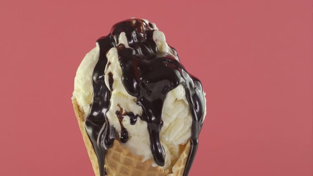 Ice cream with chocolate sauce in waffle cone over pink background
