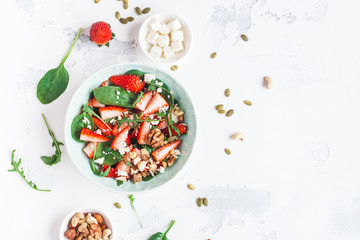 Strawberry salad. Spinach leaves, sliced strawberries, nuts, feta cheese on white background. Healthy food concept. Fat lay, top view