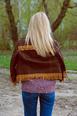 

Young sexy stylish blonde girl in nature near a river and trees in American country style in a leather jacket, sweater blue jeans and brown boots with a beautiful face and pretty eyes