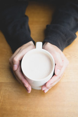 Top view of woman hand holding cup of hot cappuccino coffee on the wooden table 