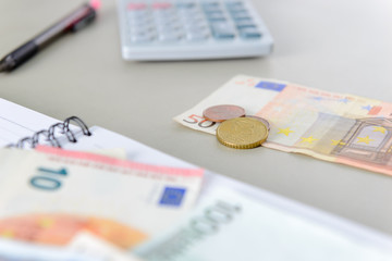 Euro money banknotes and coins counting with calculator, note book and pen on desk