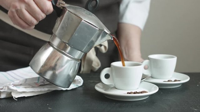 Side view of woman in the apron pouring fresh hot coffee in two small cups