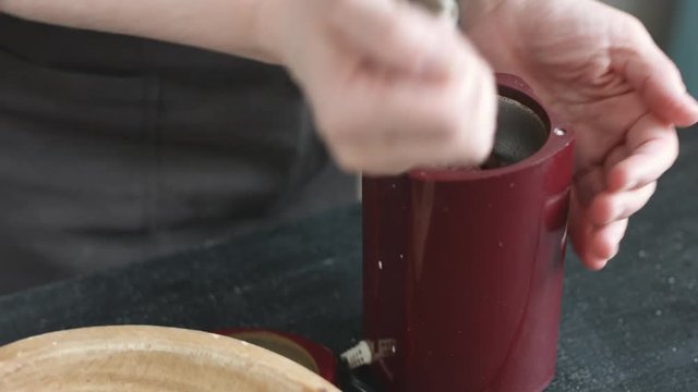 Side view of woman in the apron pours coffee beans into the grinder