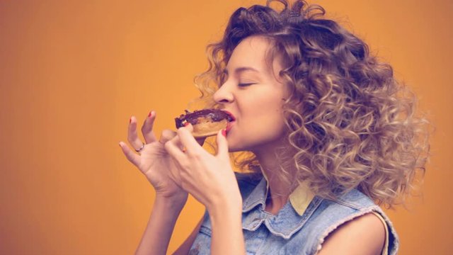 girl bites off a piece of donut with chocolate