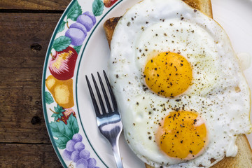 Two fried eggs on toast in plate on wooden table