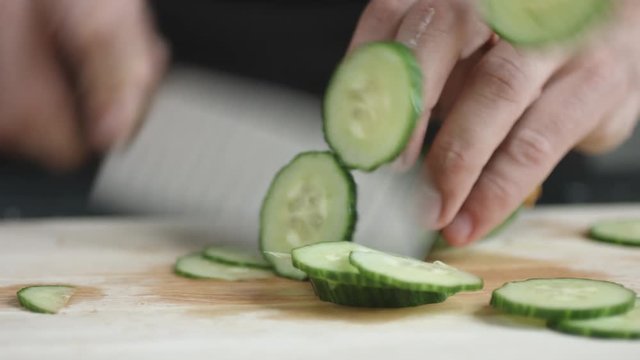 Front view of yong man cook cut thin slices of green organic cucumber with knife on cutting Board. Closeup shot with natural light