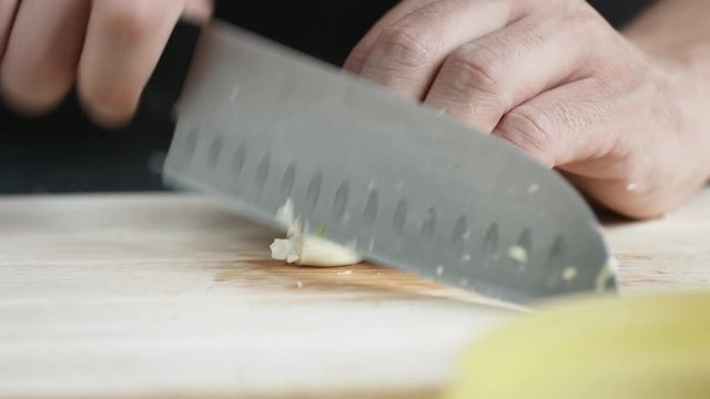 Front view of yong man cook cut thin slices of garlic with knife on cutting Board. Closeup shot with natural light