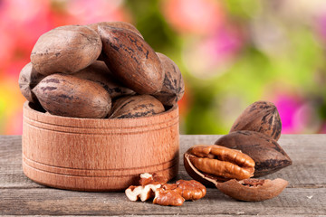 pecan nuts in a wooden bowl on the old board with blurred garden background
