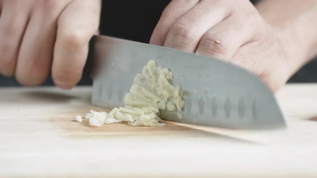 Front view of yong man cook cut thin slices of garlic with knife on cutting Board. Closeup shot with natural light