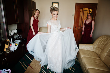 Blonde bride with bridesmaids wear on red dress at room on morning wedding day.