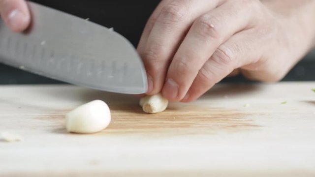 Front view of yong man cook cut thin slices of garlic with knife on cutting Board. Closeup shot with natural light