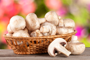 Champignon mushrooms in a wicker basket on wooden table with blurry garden background