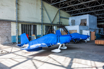 Two shrouded small sports aircraft in a hangar