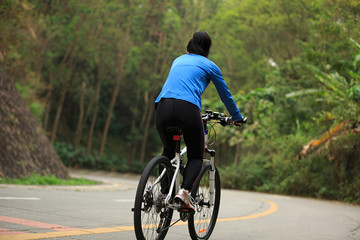 Obraz premium Young woman riding mountain bike downhill on forest trail