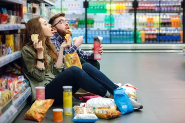 Poster Couple sitting on the supermarket floor and eating snacks © Drobot Dean