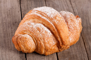 croissant sprinkled with powdered sugar on old wooden board