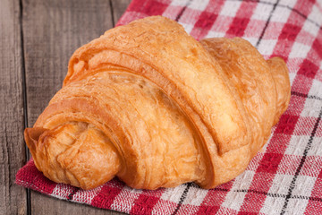 One croissant on a wooden table with a napkin
