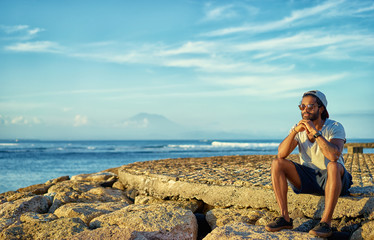 Relax and dreaming. Outdoor portrait of thoughtful young african man sitting near the sea.