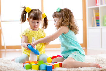 Children playing together. Toddler kid and baby play with blocks. Educational toys for preschool and kindergarten child. Little girls build pyramid toys at home or daycare.