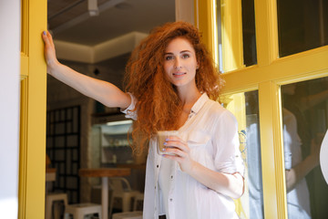 Fototapeta na wymiar Smiling red hair woman standing and holding cup of coffee