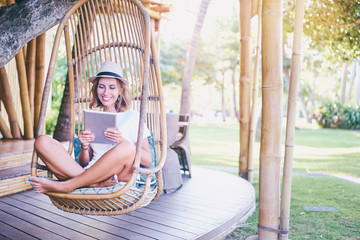 Relaxation and technology. Pretty young woman using tablet computer sitting on swing outdoors.