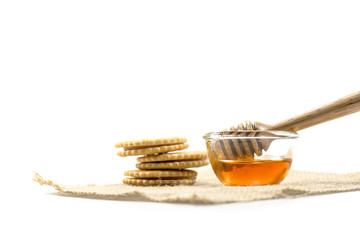 the Honey dipper and fragrant honey into a transparent bowl with cracker isolated white background.