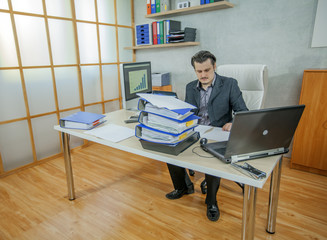 There are lots of folders in the businessman's office. He looks worried about the work that he needs to do.