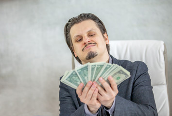 A businessman is having a smile on his face when looking at all the money in his hands. 