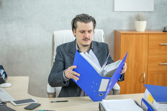 A young businessman is opening a big blue folder to check something in it.