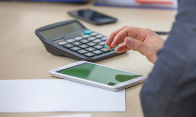 A young man is checking his smart phone. There is a calculator on a table, too.