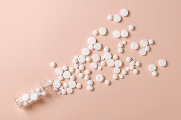 White pills spilling out of a toppled transparent glass pill bottle