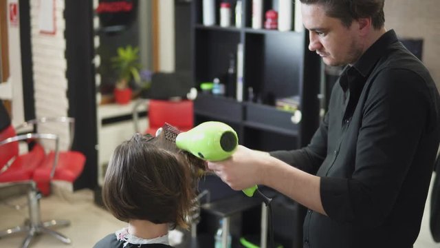 Professional hairdresser is drying hair of young attractive woman in beauty salon. Shot in 4k