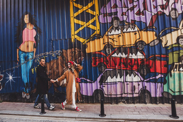 Happy couple walking at street with colorful painted walls with graffiti