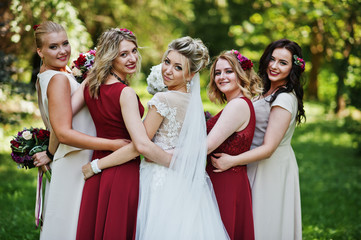 Gorgeous blonde bride with four bridesmaids at red and beige dresses outdoor.