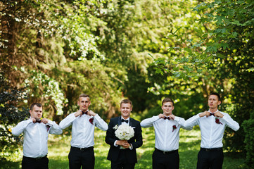Fashionable groom with four best mans at bow ties outdoor.