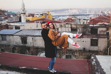 Funny stylish couple having fun on roof. Red beret and beige coat