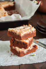 Stack of brownie cheesecake squares on a parchment paper on a wooden background. Close up.