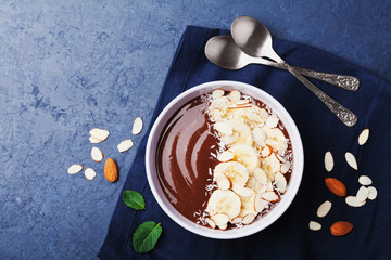 Chocolate banana almond coconut smoothie bowl on stone table top view. Healthy breakfast or dessert. Flat lay.